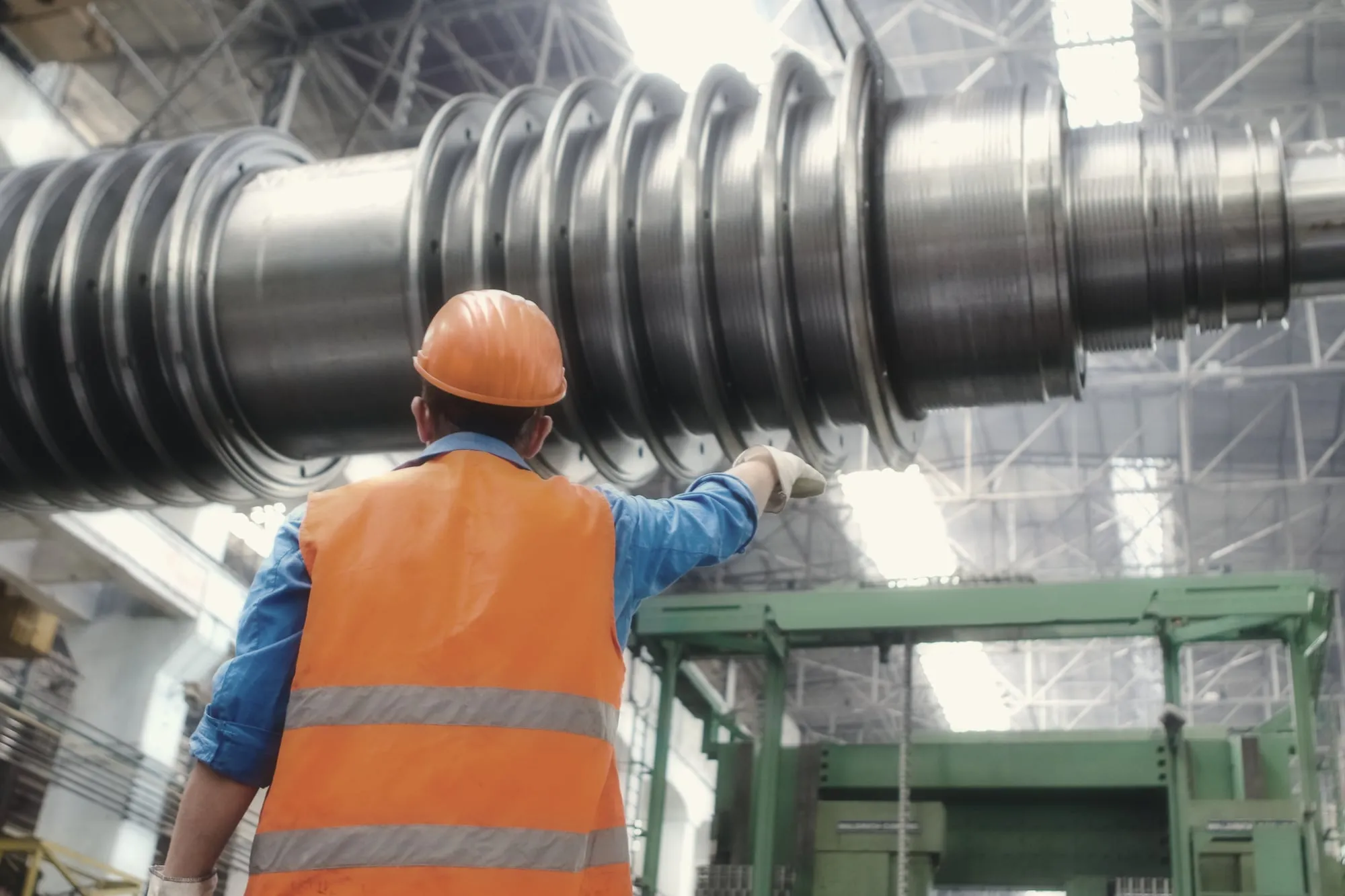 Een ingenieur met helm wijst naar een turbineas in de fabriekshal