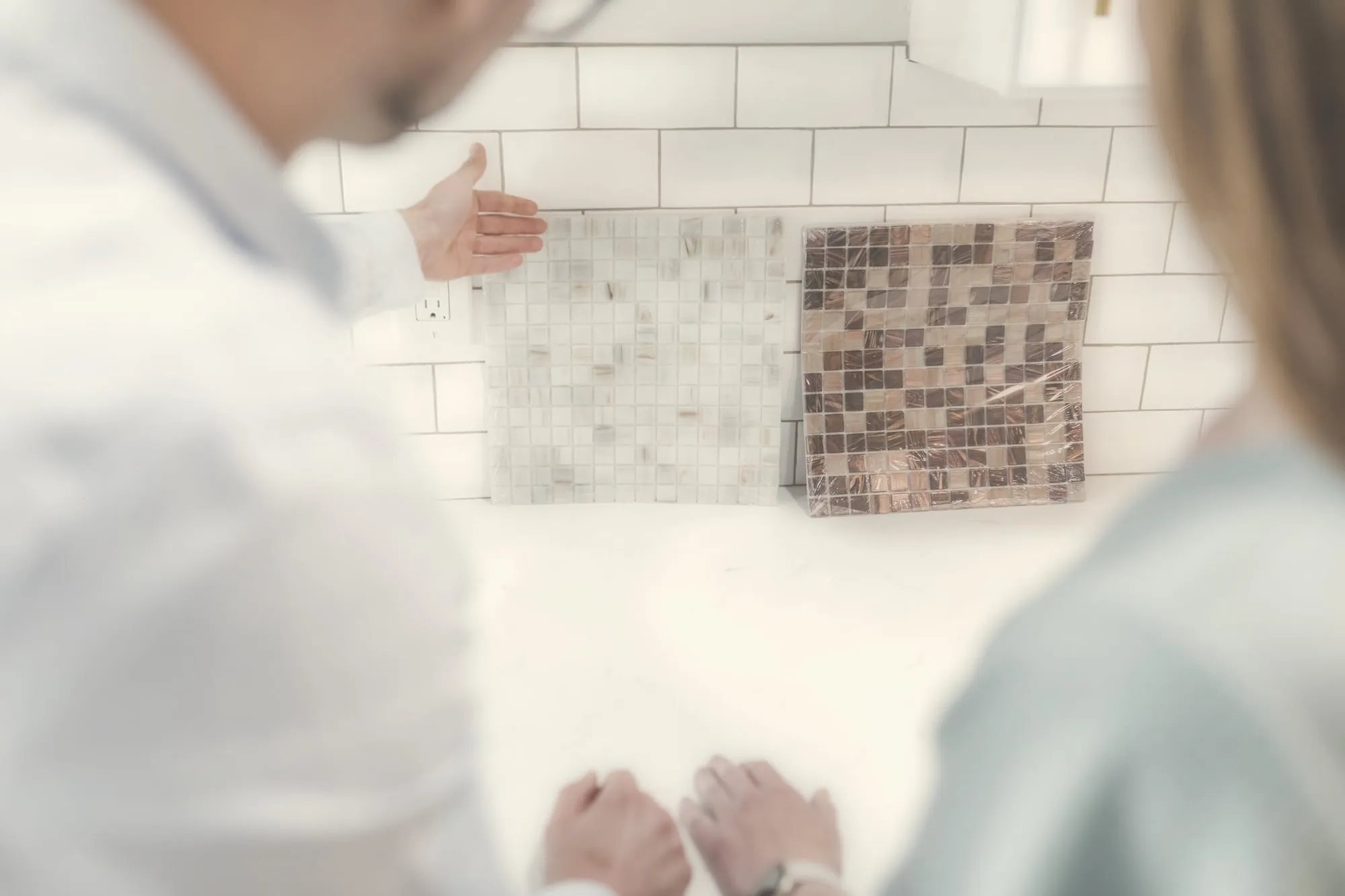 A couple looks at backsplash tile samples over a kitchen worktop