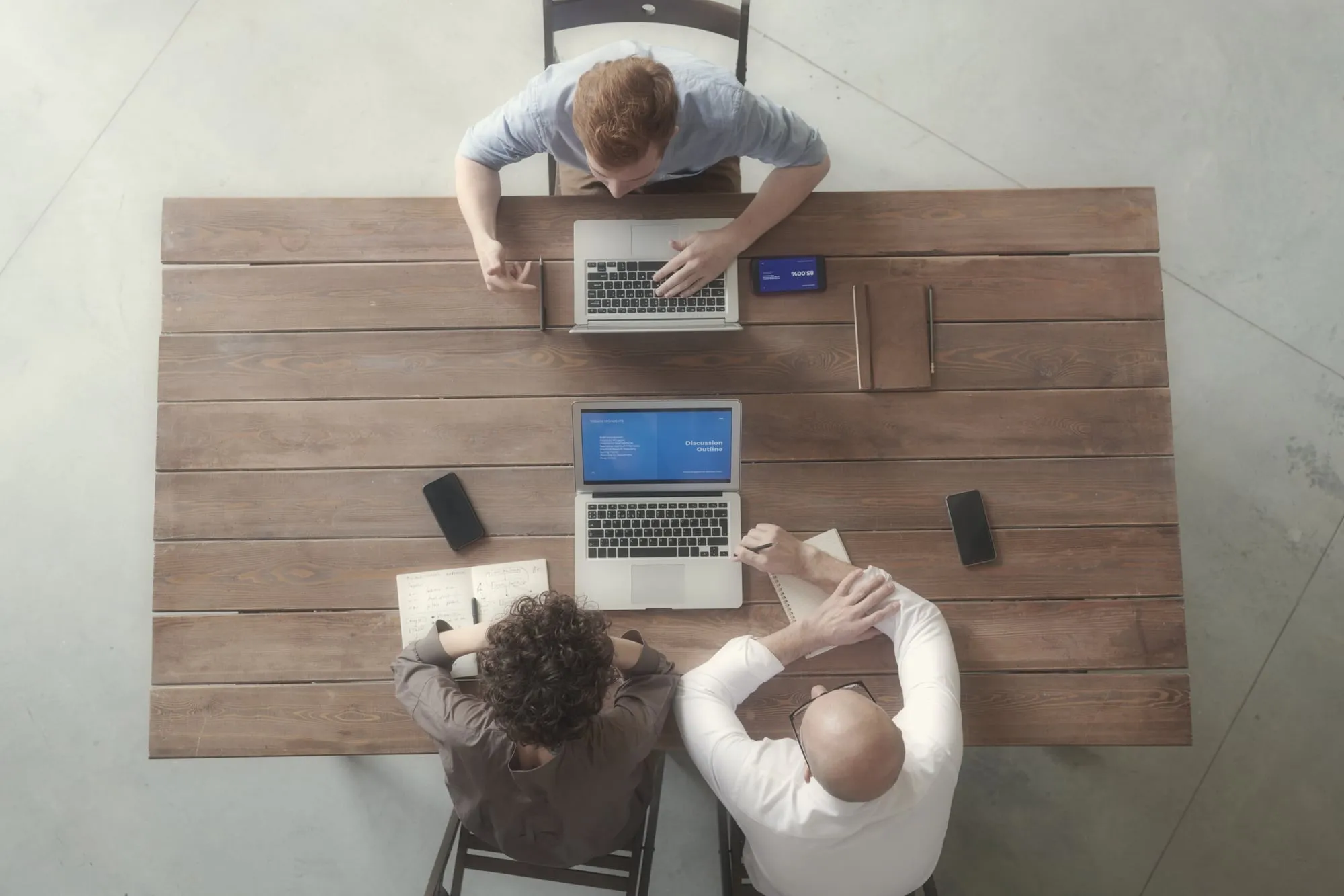 Three people working on laptops around a wooden table, seen from above
